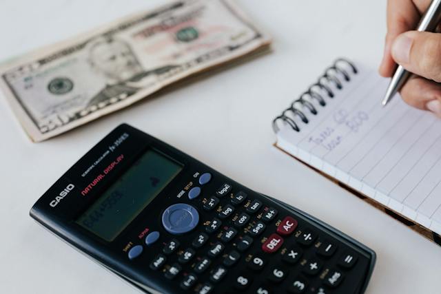a calculator stack of cash and a notepad on a desk